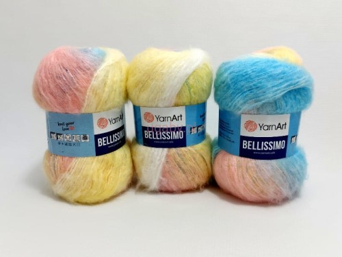Trzy motki puszystej włóczki YarnArt Bellissimo numer koloru 1420 w tęczowych odcieniach pastelowego błękitu, różu i żółci na jasnym tle.